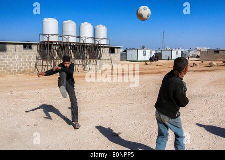 Zaatari Camp, Al Mafraq, Jordanien. 8. Februar 2014. Die Flüchtlinge von Zaatari - eine Partie Fußball oder Futbol, ist ein regelmäßiger Anblick innerhalb des Lagers. Hinter den Spielern ist einer von Dutzenden von provisorischen Toiletten mit Wassertanks, die Lagerverwaltung für Sanitär regelmäßig füllen muss. In der jordanischen Wüste liegt 10 Kilometer von der syrischen Grenze ein Flüchtlingslager Zaatari genannt. Es ist Heimat von mehr als 110.000 Vertriebene, die den Krieg in Syrien seit Juli 2012 geflohen sind. Die meisten dieser Flüchtlinge sind aus der südlichen Region von Daraa, wo die Kämpfe zu den schlechtesten in der syrischen C gesehen hat Stockfoto