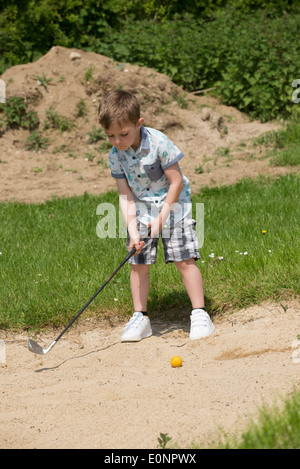 Kleiner Junge im Alter von 5 Jahren und ein begeisterter Golfer aus einem Bunker mit einem speziell senken große Golf-Club spielen. Hampshire, England Stockfoto