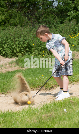 Kleiner Junge im Alter von 5 Jahren und ein begeisterter Golfer aus einem Bunker mit einem speziell senken große Golf-Club spielen. Hampshire, England Stockfoto