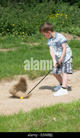 Kleiner Junge im Alter von 5 Jahren und ein begeisterter Golfer aus einem Bunker mit einem speziell senken große Golf-Club spielen. Hampshire, England Stockfoto