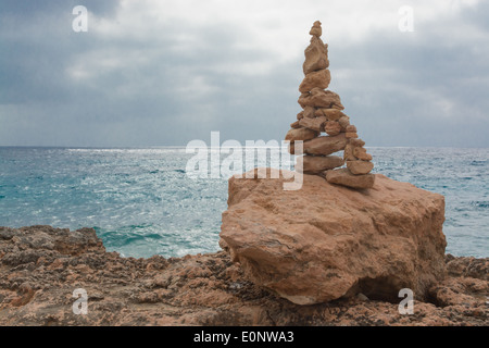 Einsame symbolische Cairn Felsenturm mit Blick auf eine stimmungsvolle dunkle Meer am Cap Salines im Oktober. Mallorca, Balearen, Spanien. Stockfoto