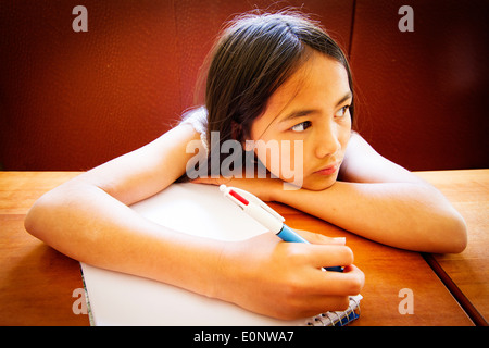 Junge Englisch / Thai Mischlinge Mädchen zeichnen mit einem Stift in einem Malbuch an einem Tisch in einem restaurant Stockfoto