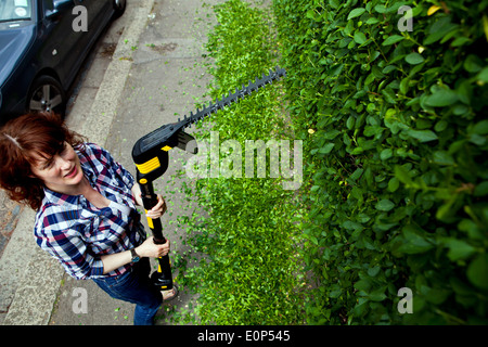 Frau trimmen Hecke mit einem schnurlosen elektrischen Heckenschere Stockfoto