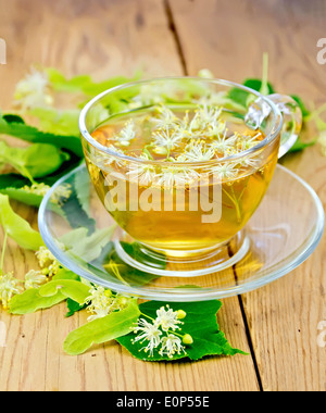 Kräutertee aus Lindenblüten in eine Glasschale, frische Lindenblüten auf einem Holzbrett Stockfoto