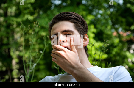 Müde oder gelangweilt junger Mann in einem Park, Gähnen, den Mund mit der hand Stockfoto