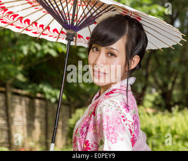 Asiatin in einem Kimono in einem japanischen Garten hält einen Regenschirm Stockfoto