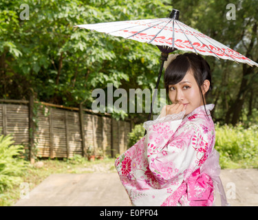 Asiatin in einem Kimono in einem japanischen Garten hält einen Regenschirm Stockfoto