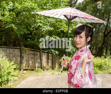 Asiatin in einem Kimono in einem japanischen Garten hält einen Regenschirm Stockfoto