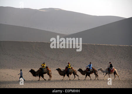 (140519)--DUNHUANG, 19. Mai 2014 (Xinhua)--Touristen fahren Kamele, wie sie die Mingshashan (wörtlich "Gesang-Sand-Berg") und Crescent Lake, Aussichtspunkt eine Oase in der Wüste Gobi in Dunhuang, Nordwesten Chinas Provinz Gansu, 18. Mai 2014 zu besuchen. (Xinhua/Zhang Xiaoliang) (Lmm) Stockfoto
