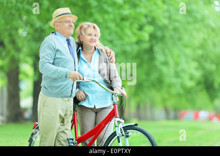 Älteres paar umarmt und schob ein Fahrrad im park Stockfoto