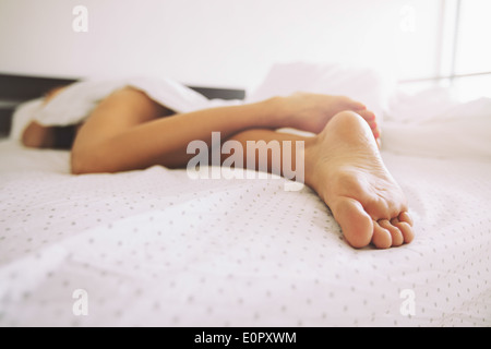 Junge Frau im Bett zu Hause mit Fokus auf die Beine. Füße der Frau auf dem Bett liegend. Stockfoto