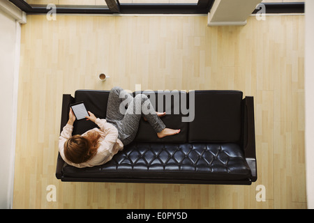 Draufsicht der junge Dame sitzt auf einer Couch mit digital-Tablette. Weibliche entspannend auf Sofa mit einem e-Reader in ihrer Wohnung. Stockfoto