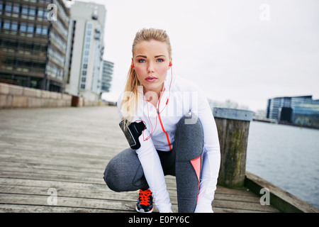 Fitness-Frau auf der Promenade zu hocken, ihr Blick in die Kamera Schnürsenkel zu binden. Überzeugt junge weibliche Jogger Training im Freien. Stockfoto
