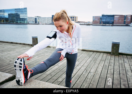 Passen Sie die junge Frau vor einem Lauf dehnen. Junge weibliche Läufer dehnen Sie ihre Muskeln vor einer Trainingseinheit Stockfoto