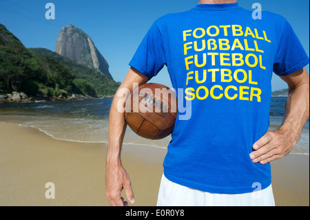 Brasilianische Fußballspieler in Multi Sprache Nachricht T-shirt Holding Vintage Fußball rot Strand Rio de Janeiro Brasilien Stockfoto