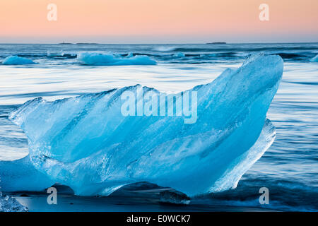 Eisblock am schwarzen Strand wird durch das Meer umspült, Gletscherlagune Jökulsárlón, Gletscher Vatnajökull, Austurland Stockfoto