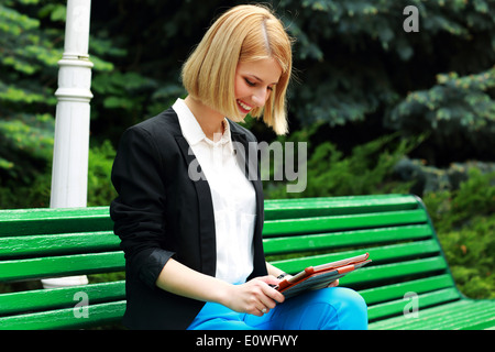 Junge fröhliche Frau, die auf der Straße Bank mit Tisch Computer sitzen Stockfoto