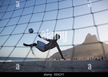 Ein Fußballer erzielt akrobatisch ein Tor aus einem Bicyclette Overhead Fußball Kick am Strand von Ipanema in Rio De Janeiro, Brasilien Stockfoto