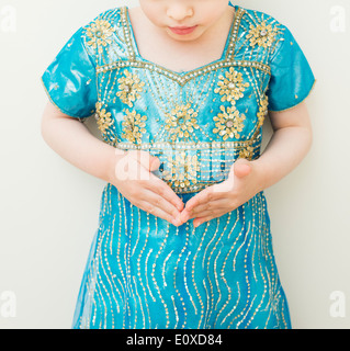 Kleines Mädchen im blauen Kleid blickte auf ihre Hände, ernst und konzentriert. Stockfoto