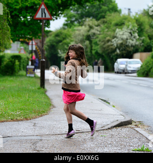 Junge weiße Mädchen mit langen braunen Haaren in einem rosa Rock und braune Jacke auf der Straße im Regen tanzen. Manningtree, UK Stockfoto