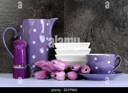 Moderne lila und weißen Tupfen Küche mit großen Servierplatte Teller, Besteck und Geschirr gegen schwarze Schiefer Tisch. Stockfoto