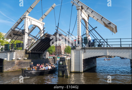 Amsterdam Magere Brug, Skinny Bridge, kleines Boot vorbei Zugbrücke. Ein Bridgeman auf Fahrrad schließt die Klappbrücke Unentschieden.