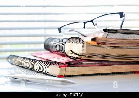 Stapel der Office-Ordner mit Brille und Kugelschreiber vor einem Fenster Stockfoto
