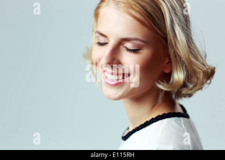 Closeup Porträt einer lächelnden Frau mit geschlossenen Augen auf grauem Hintergrund Stockfoto
