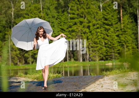 5. Juni 2010 - 5. Juni 2010 - Happy romantische Frau mit Sonnenschirm in der Sonne, weißen Kleid, zu Fuß in Wasser Stockfoto