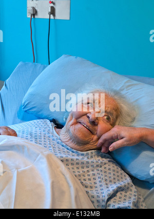 ÄLTERE DAME PFLEGEBETT LÄCHELND BERÜHREND zufrieden lächelnd Ältere Alterswarnung Ältere Dame sicher in Pflegebett mit beruhigender Hand der Pflegerin Krankenschwester Stockfoto