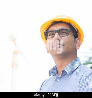 Porträt eines asiatischen indischen Ingenieur wegsehen, stehen vor Baukran, prüfen den Fortschritt des Projekts. Stockfoto