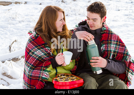 Junges Paar beim Picknick am Valentinstag in einem verschneiten Park. Stockfoto