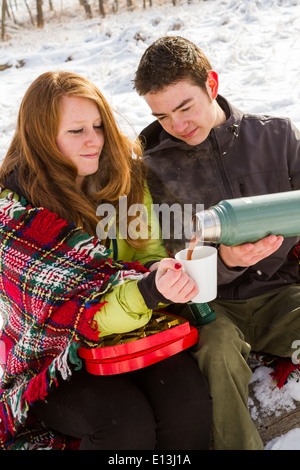 Junges Paar beim Picknick am Valentinstag in einem verschneiten Park. Stockfoto