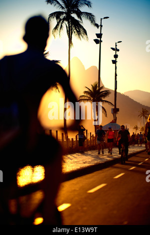 Aktive Silhouetten von Menschen radeln und Wandern am Sonnenuntergang Radweg in Ipanema Strand Rio de Janeiro Brasilien Stockfoto