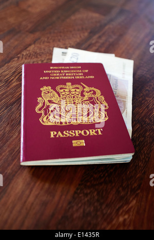 Ein alter EU-Stil vor dem Brexit burgunderrot UK Passport mit alten GBP Sterling Banknoten auf einer dunklen Holz-Tischplatte. Stockfoto