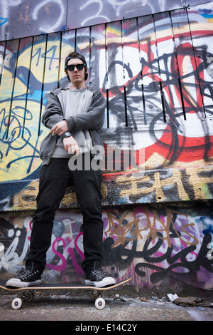 Kaukasische Teenager auf Skateboard durch Graffitiwand Stockfoto