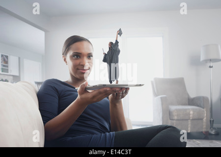 Schwarze Frau beobachtete Figur des graduate stehend auf digital-Tablette Stockfoto