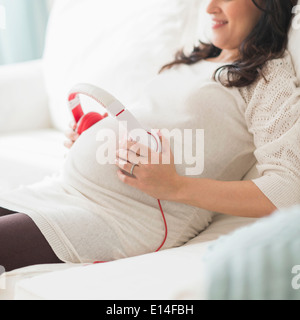 Hispanic schwangeren Bauch Kopfhörer festhalten Stockfoto