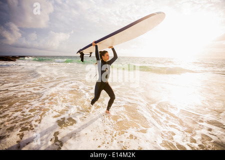 Kaukasische Surfer tragen Board in Wellen Stockfoto