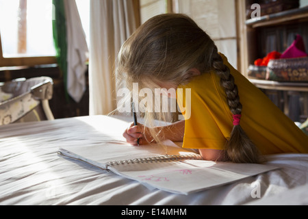 Kaukasische Mädchen Zeichnung im Notebook auf Bett Stockfoto