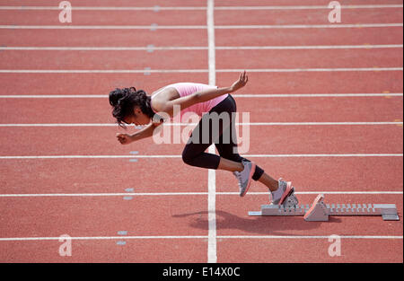 Sportliche junge Frau, die ausgehend vom Startblock auf Laufband laufen Stockfoto