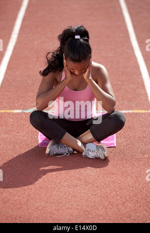 Sportliche junge Frau, meditieren, sitzen auf Rennstrecke, immer geistig bereit Stockfoto