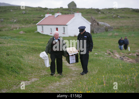 Vorsitzender Offizier Hugh O'Donnell und Garda Officer p.j. McHugh tragen die Wahlurne auf der Insel Innishfree, County Donegal, Stockfoto