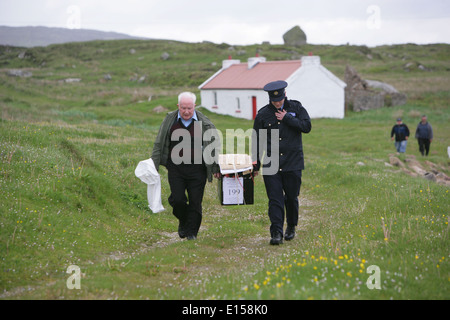 Vorsitzender Offizier Hugh O'Donnell und Garda Officer p.j. McHugh tragen die Wahlurne auf der Insel Innishfree, County Donegal, Stockfoto