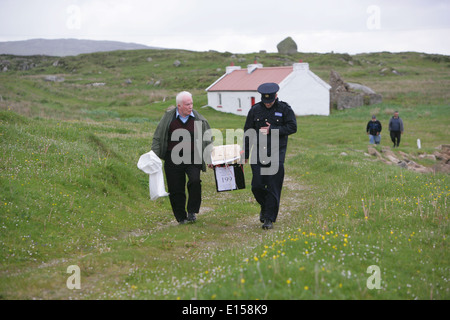 Vorsitzender Offizier Hugh O'Donnell und Garda Officer p.j. McHugh tragen die Wahlurne auf der Insel Innishfree, County Donegal, Stockfoto