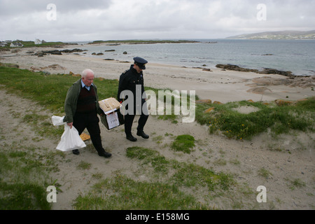 Vorsitzender Offizier Hugh O'Donnell und Garda Officer p.j. McHugh tragen die Wahlurne auf der Insel Innishfree, County Donegal, Stockfoto