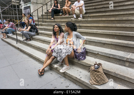 2 junge hübsche schwarze Freunde sitzen auf Stufen des Federal Hall in lower Manhattan unter anderen Menschen besuchen oder arbeiten im Bereich Stockfoto