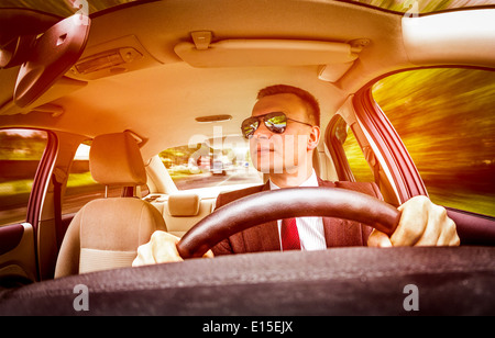 Mann in einem Anzug und Sonnenbrille auf einer Straße im Auto fahren. Stockfoto