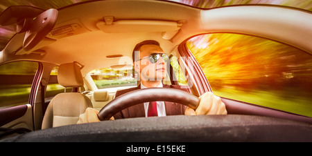 Mann in einem Anzug und Sonnenbrille auf einer Straße im Auto fahren. Stockfoto