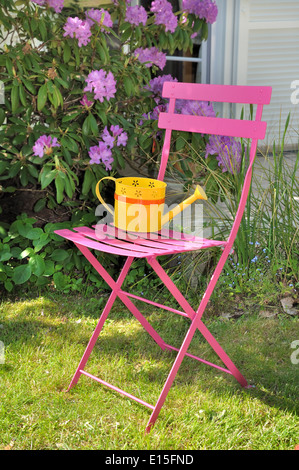 gelbe Gießkanne auf einem rosa Stuhl im Garten Stockfoto